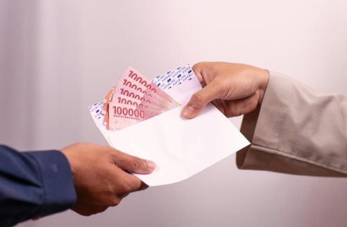 Hands giving and receiving Indonesian rupiah in an envelope, symbolizing financial transaction.